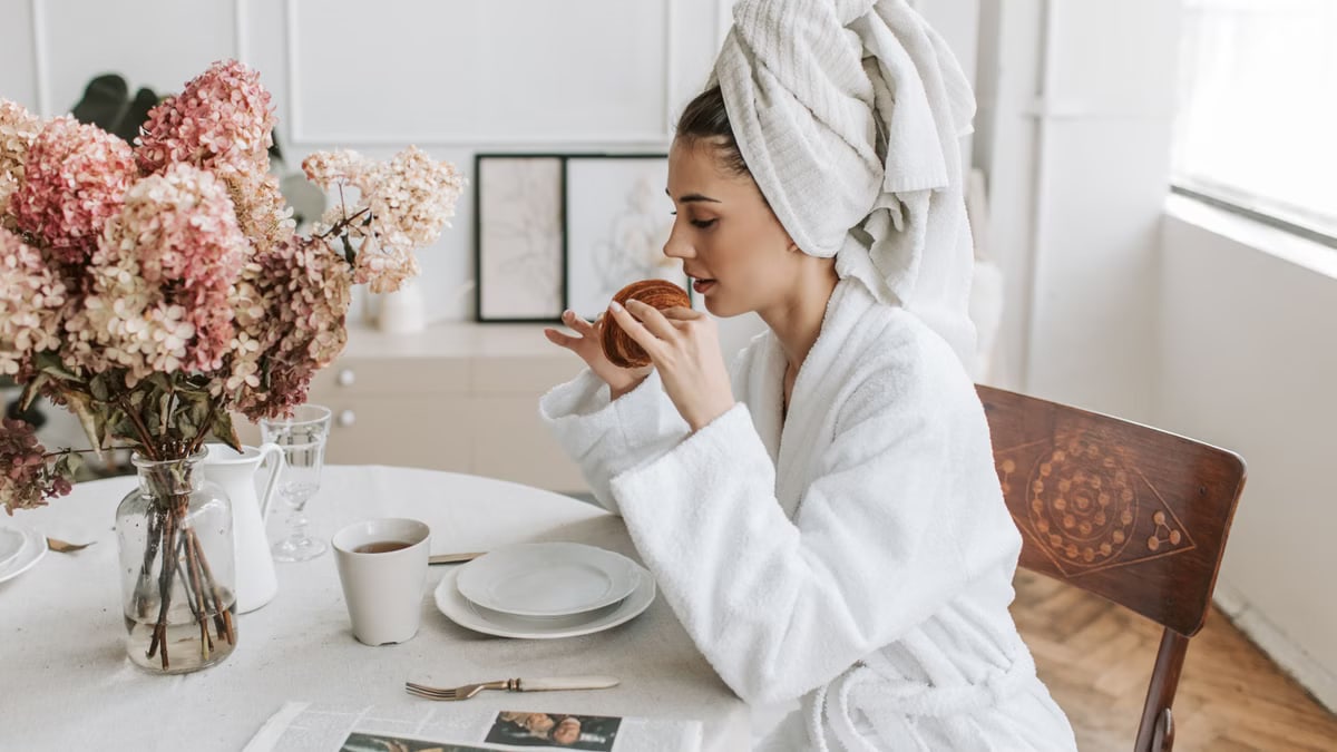 Cozy morning scene with a woman enjoying a croissant and coffee at a dining table indoors.